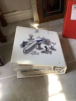 Photo of the large white hardcover binder containing comic books, showing the binder closed with comic-related imagery on top.