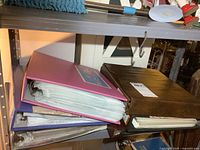 Six assorted-color binders stacked on metal shelving