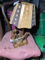 Full view of the vintage wooden folk art lamp showing wooden block-patterned shade and carved figure base on a pink cloth surface.
