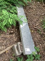 Long granite slab resting on paver stones, surrounded by natural outdoor foliage.