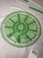 Top-down view of a green glass platter showing circular pattern with pineapple motifs and beaded edge.