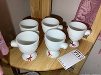Photo of five white milk glass hen-shaped goblets arranged on a wooden shelf, showing their overall shape and design.
