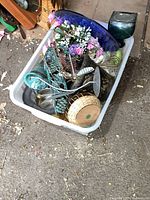Photo of white plastic container filled with home decor items including baskets, metal decorative items, artificial flowers, and glass bottles.