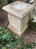 Front and side view of a large square pedestal with decorative panels and dirt on the surface.