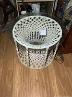 Front angle view showing metal framed round macrame table with removable glass top, sitting on wooden floor.