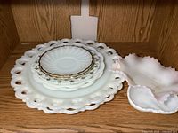 Top view of stacked milk glass plates and dishes with decorative rims and gold accents.