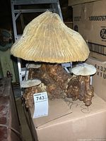 Front and side view of the resin mushroom lamp showing the large mushroom cap with ridged texture and smaller mushroom caps at the base with textured bark and moss detail.