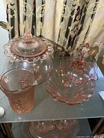 Top view of pink glass set showing snack tray, footed bowl, pitcher, and lidded dish on shelf.