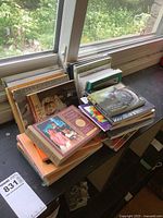 A wide view showing a large stack of various postcard books and booklets placed on a window sill, illustrating the quantity and types of books included in the lot.