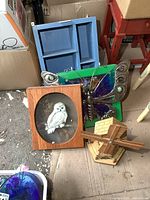 Photo showing wooden windmill, framed owl shadow box, metal butterfly, and blue wood shelf arranged together on floor