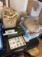 Table setup with brown paper bags and plastic bag containing loose stamps, and stamp albums stacked
