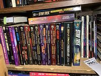 Books arranged tightly on wooden shelf, showing various Star Trek series softcovers with colorful spine designs and Pocket Books logos.