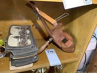 Stack of vintage stereo cards with black and white images next to an antique wooden stereoscope viewer on a leather chair.