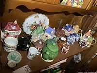 View of assorted decorative teapots, a plate, and cups arranged on a wooden shelf.
