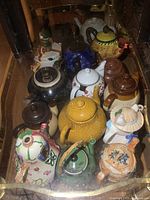 Overhead shot showing a group of fifteen assorted ceramic and porcelain teapots in different shapes, sizes, and colors arranged together.