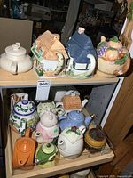 Photo showing top two shelves with a variety of ceramic teapots shaped like cottages, fruit baskets, and various floral patterns.
