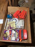 Drawer contents with three vintage red View-Master viewers and multiple View-Master reels/discs in packaging and loose, including instruction pamphlets and promotional materials.
