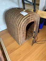 Wicker pet carrier showing left side and front curved doorway with partially open door and latch.