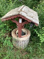Wishing well with wooden lattice base, weathered red paint posts, shingled roof showing wear.