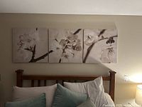 Three piece floral print wall art set mounted on a wall above a bed frame.