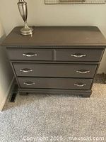 Photo of a dark wooden bedroom dresser with four drawers and metal handles, topped with a lamp which is not included in the sale.