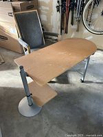 Photo showing a wooden desk with a curved top and metal legs, accompanied by a high-backed upholstered chair with wooden armrests.