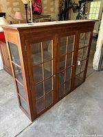 Front and side view of wooden china hutch showing glass paneled doors and wood finish.