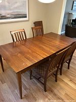 Rectangular medium brown wooden dining table with four matching high-back chairs, table expanded with leaves.