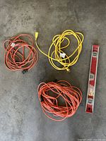 Photo of three extension cords (two orange, one yellow) and one red 2-foot level on a concrete floor.