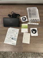 Displayed Fujitsu IX500 document scanner with power cable, installation CDs, manuals, and a protective document sleeve, all arranged on a wooden surface.