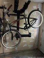 Black Nirve men's beach cruiser bicycle hanging on a garage rack. Frame, wheels, handlebars, grips, pedals, and chain guard visible. No rear rack included.