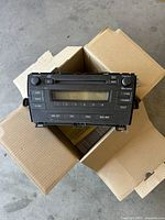 Photo of the OEM car stereo unit for 2010 Toyota Prius sitting on cardboard boxes, showing front view with buttons and display screen.