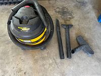 Shop-Vac wet/dry vacuum cleaner with hose and various attachments displayed on concrete floor.