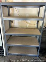 Full view of metal storage rack with four shelves against a wall.