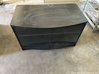 Top-down angled view of black TV stand with curved glass cabinet doors and flat top surface.