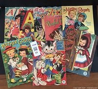 Eight children's vintage picture books arranged overlapping, showing colorful illustrated covers with girls, animals, and titles such as Nursery Rhymes, Mother Goose, and Little Red Riding Hood.