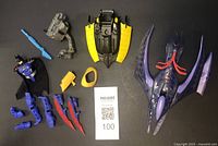 Photo of Batman-themed plastic toy parts and figures laid out on black background, showing figures, weapons, vehicle parts including a winged yellow-black piece and a purple Sea Claw vehicle.