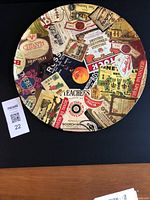 Front side of round metal tray with various vintage liquor and wine labels affixed