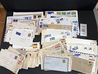 An overhead shot of a large group of assorted postal covers and envelopes arranged in loosely stacked piles, showing variety in stamps and postmarks from global locations.