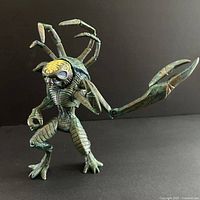 Front view of green Primagen alien figure showing detailed insectoid body, articulated limbs, and exposed brain design on the head.