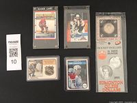 Front view of four hockey cards in protective plastic cases and one sealed hockey dollar coin in original packaging.
