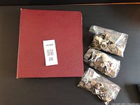 Photo of red binder with three sealed plastic bags containing various small metal detected items on side.