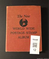 Front cover of the red vintage postage stamp album titled 'The New World Wide Postage Stamp Album' with some wear on edges.