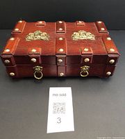 Front view of vintage wooden jewellery box, showing the detailed gold metal embellishments and brass studs along edges.