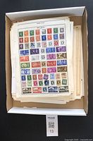 Top view of box containing approximately 100 sheets of world stamps on album pages and loose sheets.