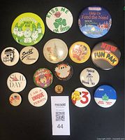 Front view of 17 vintage buttons and pins with holiday and themed designs and slogans.