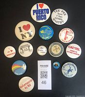 Front views of 14 vintage buttons and pins featuring place names and slogans