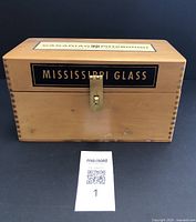 Front view of vintage wood box with Mississippi Glass painted logo and brass latch, showing dovetail corners.