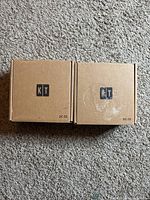 Two brown cardboard boxes labeled KT DC-33 side by side on carpet.