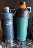 Photo showing two Stanley insulated bottles on a dark surface.